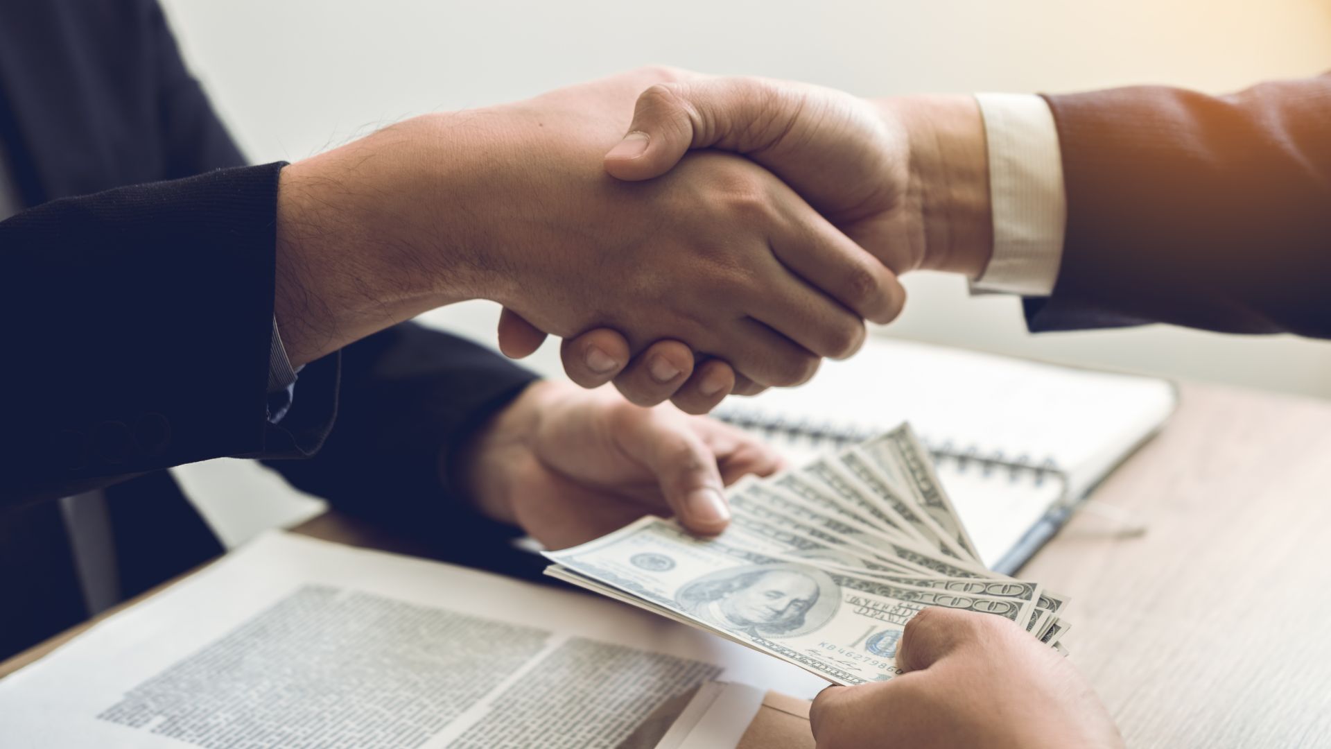 two people shaking hands over a desk and passing earnest money